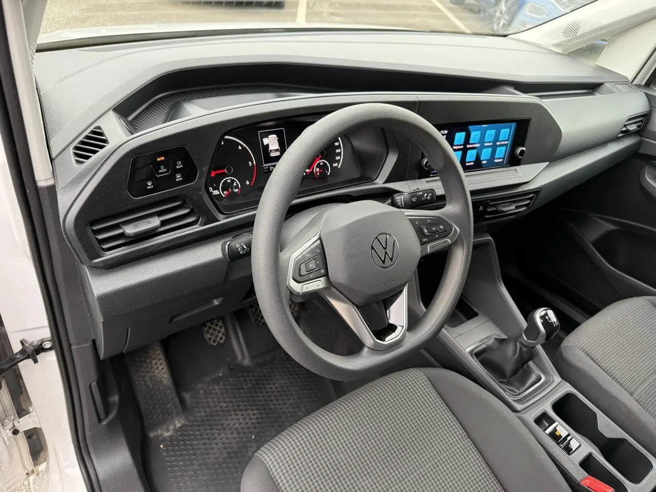 Vue intérieure du tableau de bord et volant multifonctions du Volkswagen Caddy Maxi Cargo blanc, avec écran tactile et boîte manuelle.
