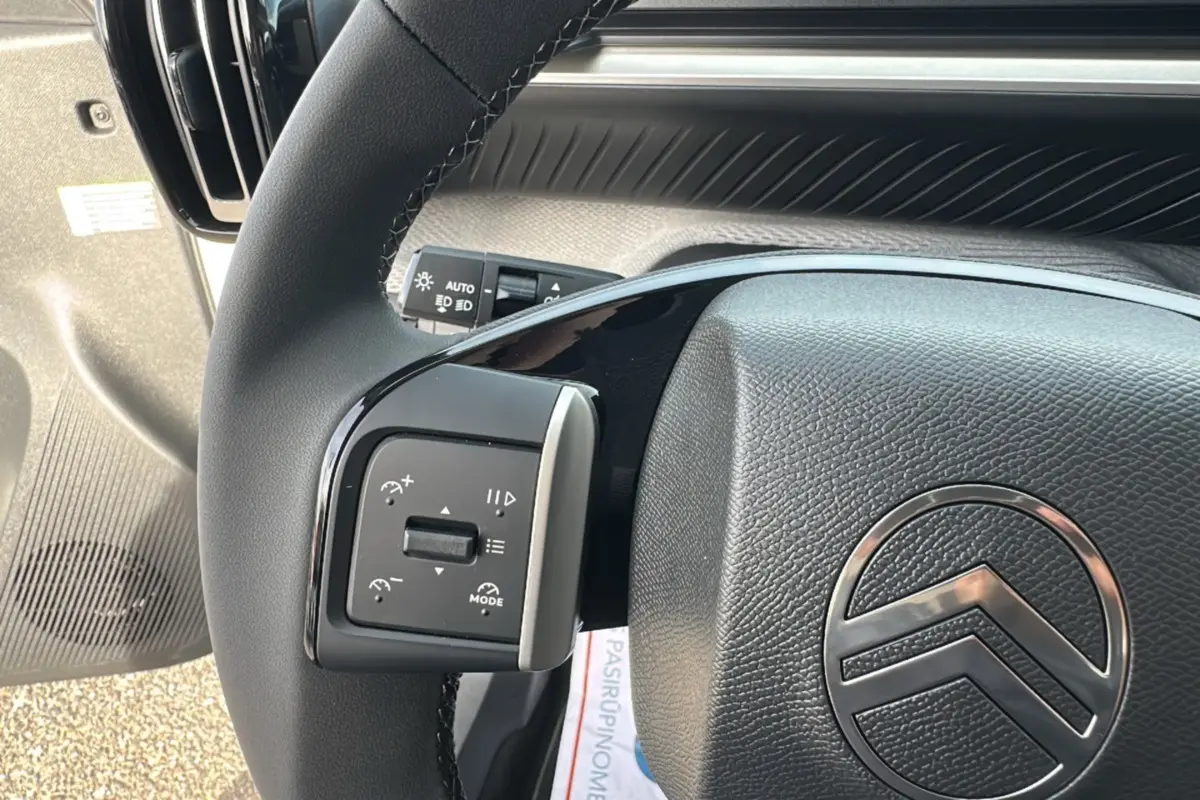 Gros plan sur le volant cuir noir de la Citroën C3 Aircross blanc banquise, avec commandes multifonctions visibles à gauche.