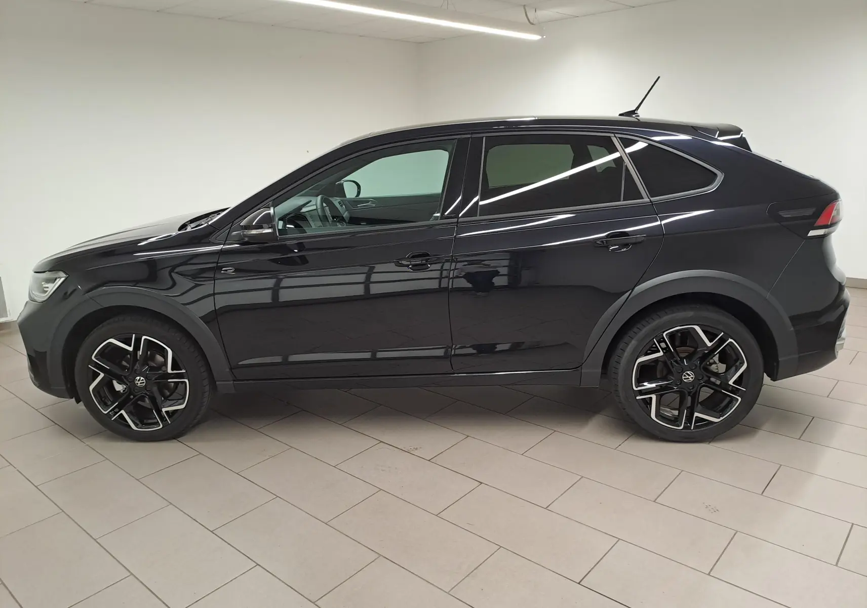 Profil côté gauche d'un Volkswagen Taigo noir intense nacré, avec jantes alliage R-Line et toit ouvrant visible.
