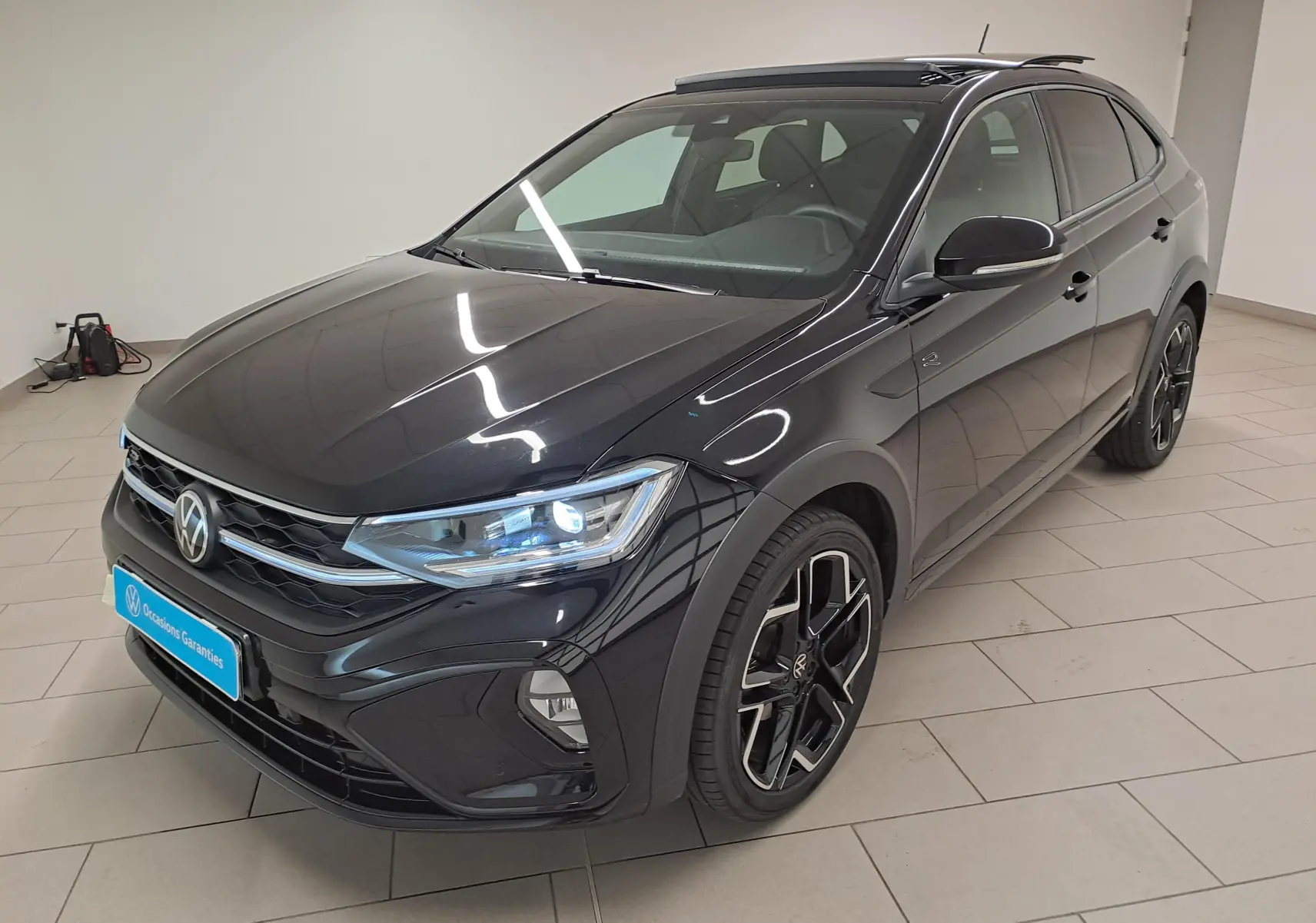 Vue 3/4 avant droit d'un Volkswagen Taigo noir intense nacré avec jantes alliage noires et phares LED allumés.