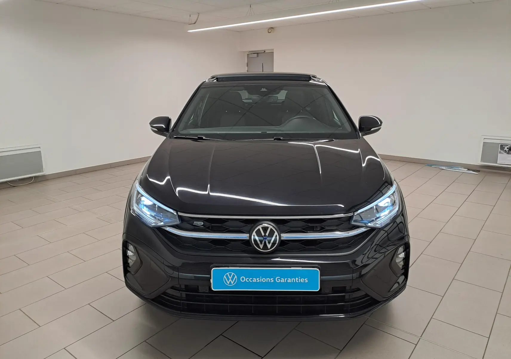 Vue avant d'un Volkswagen Taigo noir intense nacré avec calandre R-Line et toit ouvrant électrique en verre dans un showroom.