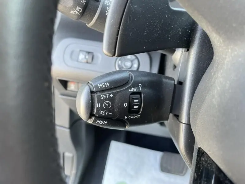 Gros plan sur la commande de régulateur de vitesse noire à gauche du volant dans l'habitacle gris du Citroën Berlingo 2018.