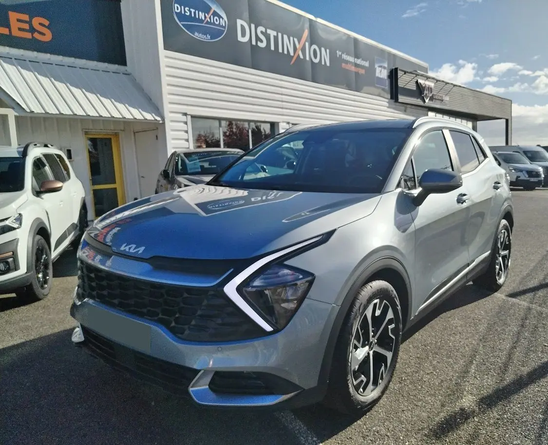 KIA Sportage gris perle en 3/4 avant droit, avec calandre noire distinctive et jantes bicolores.