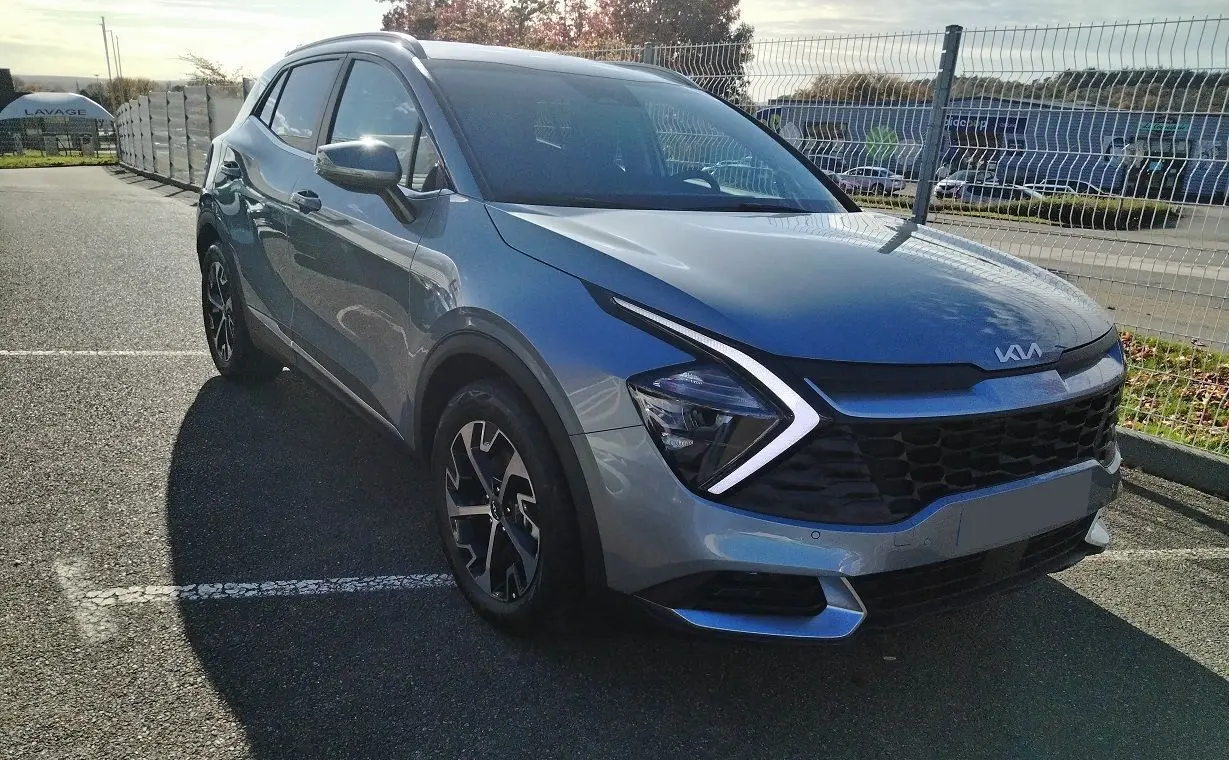 KIA Sportage gris perle en 3/4 avant droit, avec signature lumineuse en forme de flèche et calandre noire.