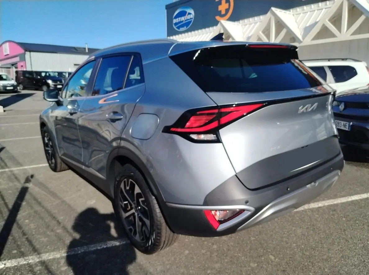 Vue 3/4 arrière droite du KIA Sportage gris perle 2025 avec feux arrière LED et jantes noires bicolores.