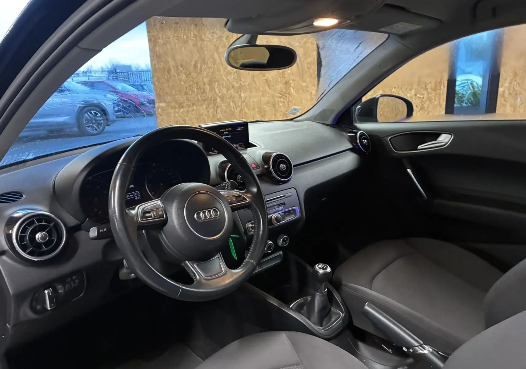 Vue intérieure côté conducteur de l'Audi A1 noire, mettant en valeur le volant multifonction, la boîte manuelle et la planche de bord épurée.