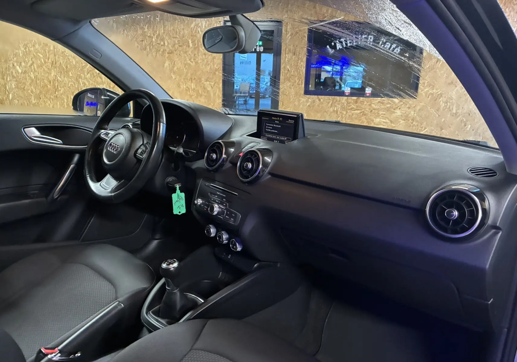 Vue intérieure côté conducteur de l'Audi A1 noire, mettant en valeur le tableau de bord, volant et levier de vitesses manuel.