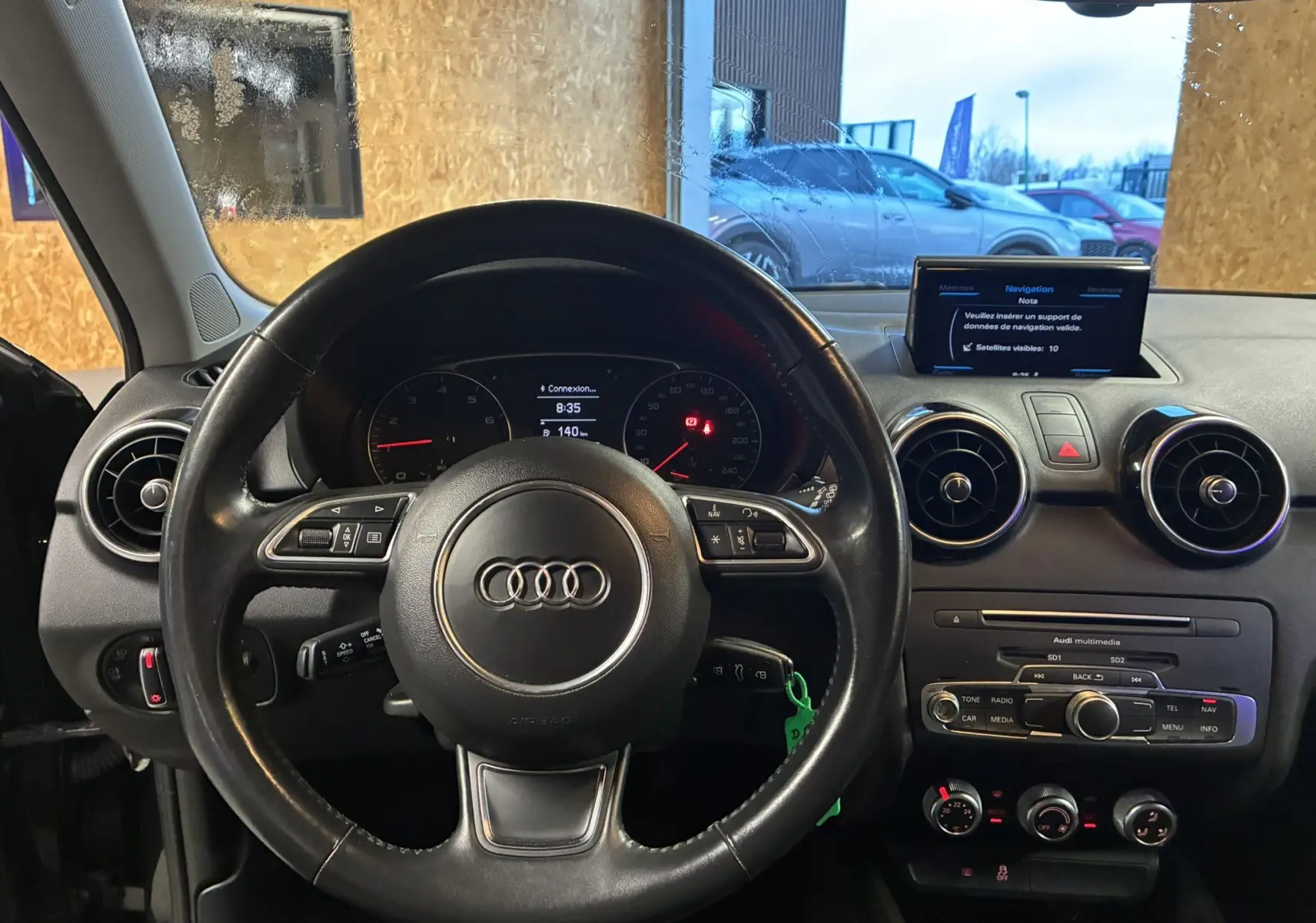 Vue intérieure centrée sur le volant noir d'une Audi A1 2016, avec tableau de bord et écran multimédia visibles.