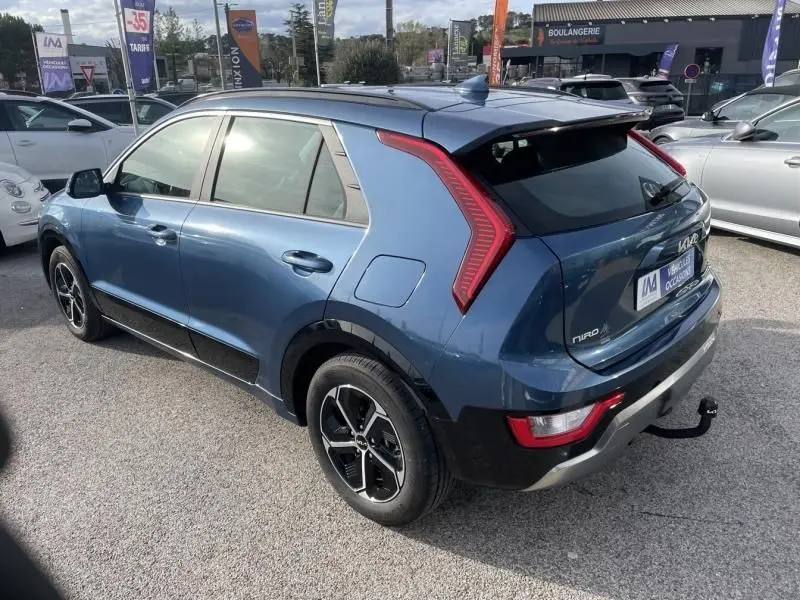 Vue 3/4 arrière droite du KIA NIRO 2024 bleu métal avec feux arrière en forme de boomerang et attelage visible.
