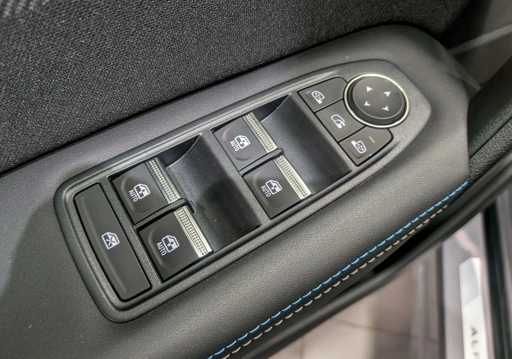Gros plan sur la commande des vitres électriques côté conducteur avec surpiqûres bleues sur la portière noire du Renault Symbioz E-Tech.