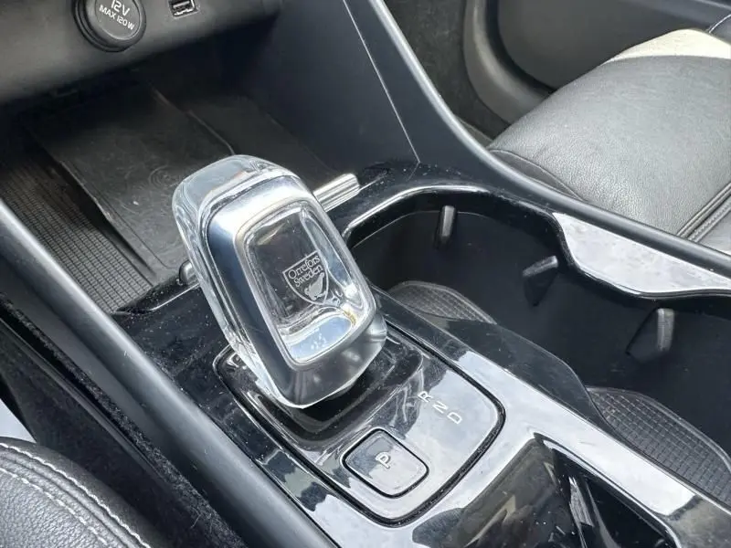 Le levier de vitesse automatique en cristal du Volvo XC40 T4 gris foncé, avec console noire et sièges en cuir visibles.