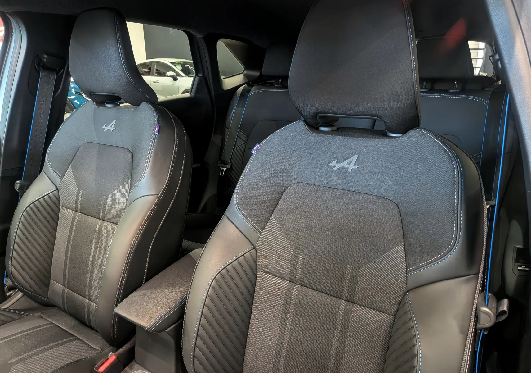 Vue rapprochée des sièges avant noirs avec surpiqûres bleues et logo Alpine sur le Renault Symbioz hybride 2026.