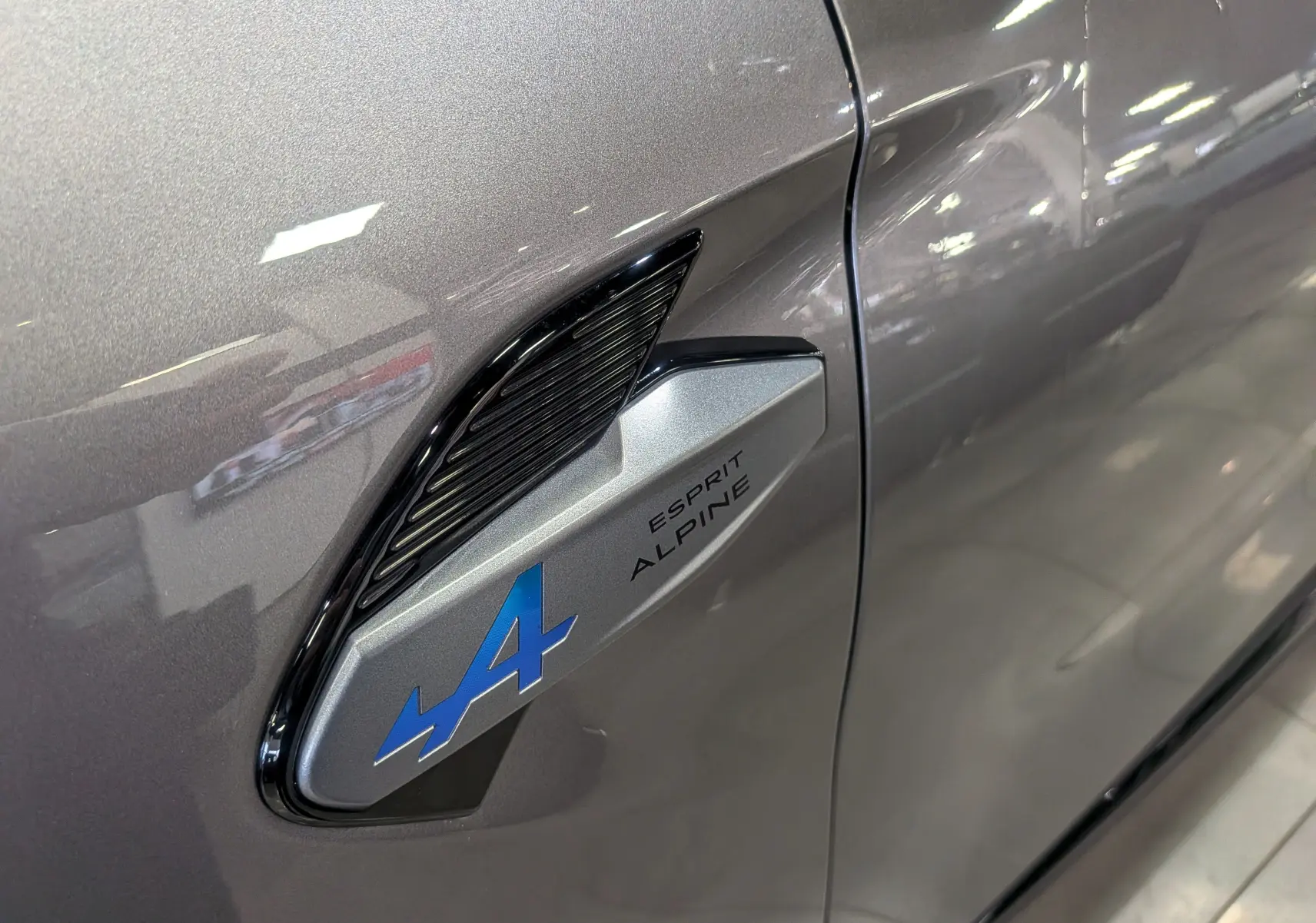 Gros plan sur l'aile avant droite gris Cassiopé du Renault Symbioz E-TECH avec logo bleu Esprit Alpine.