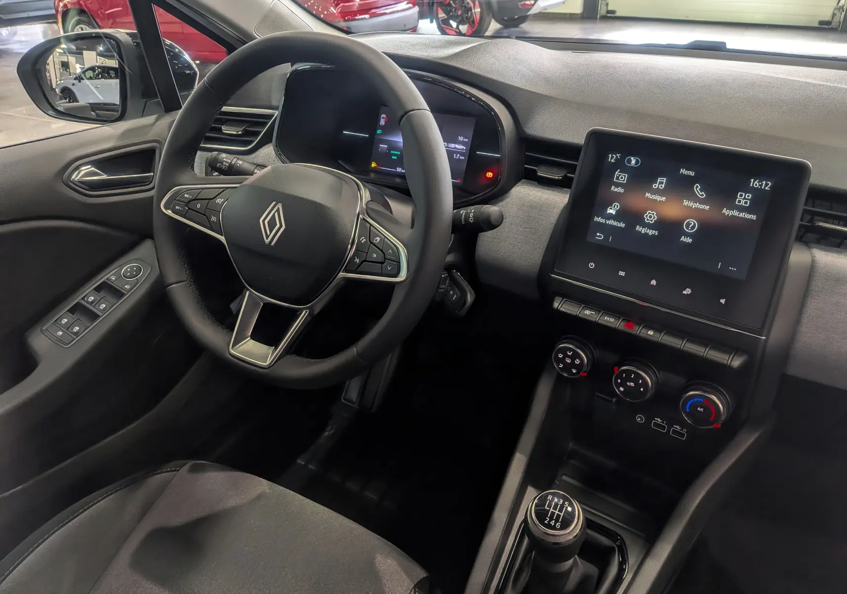 Vue intérieure côté conducteur de la Renault Clio V blanche Glacier, avec volant multifonction et écran tactile central allumé.