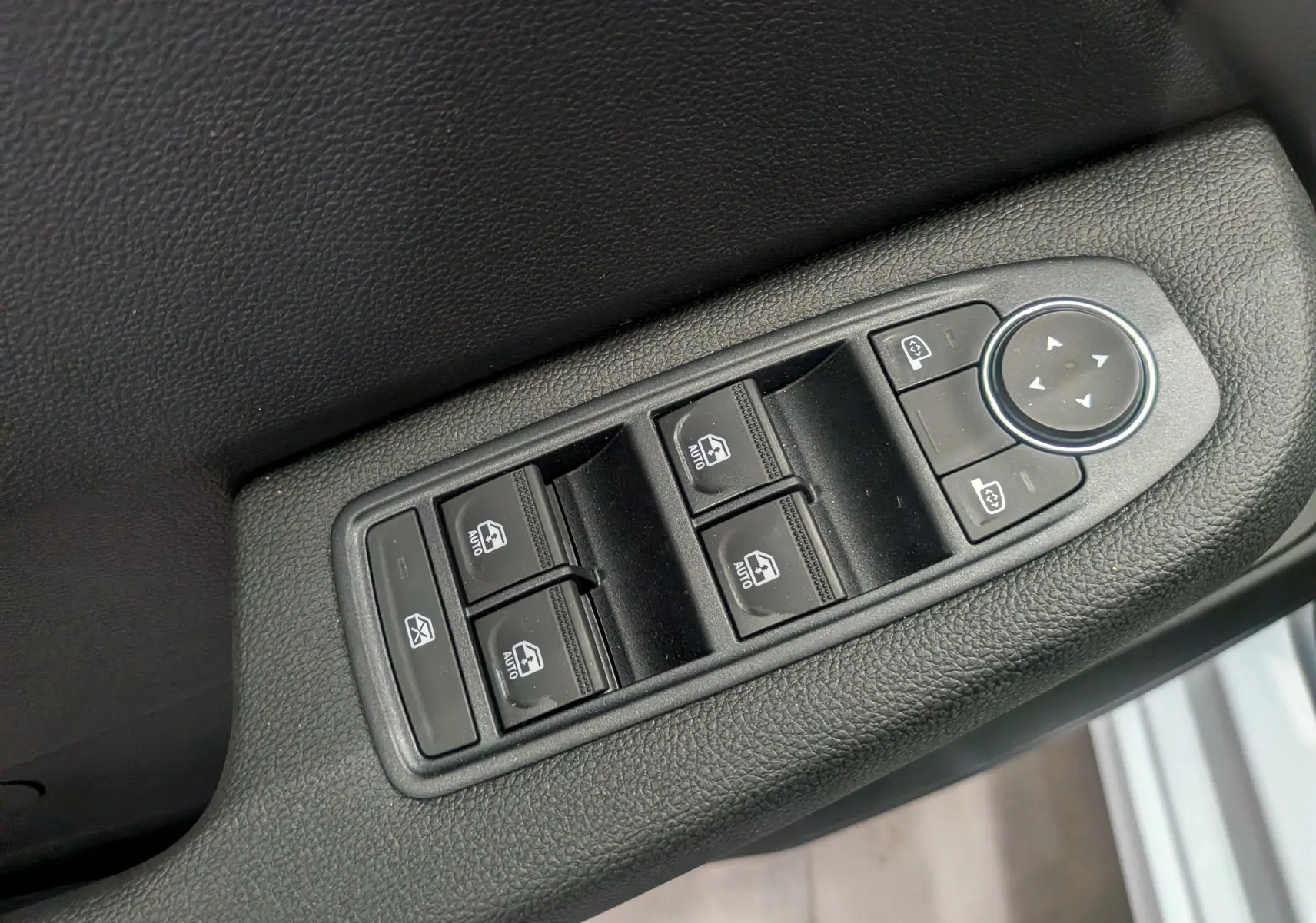 Gros plan sur les commandes électriques des vitres et rétroviseurs sur la porte intérieure côté conducteur d'une Renault Clio V.