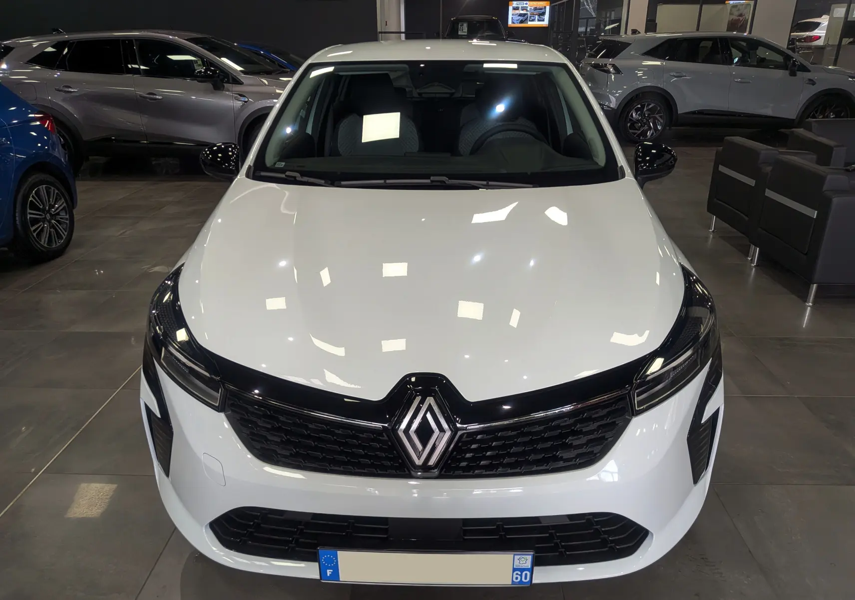 Vue avant d'une Renault Clio V Blanc Glacier en showroom, avec calandre noire et logo Renault bien visible.