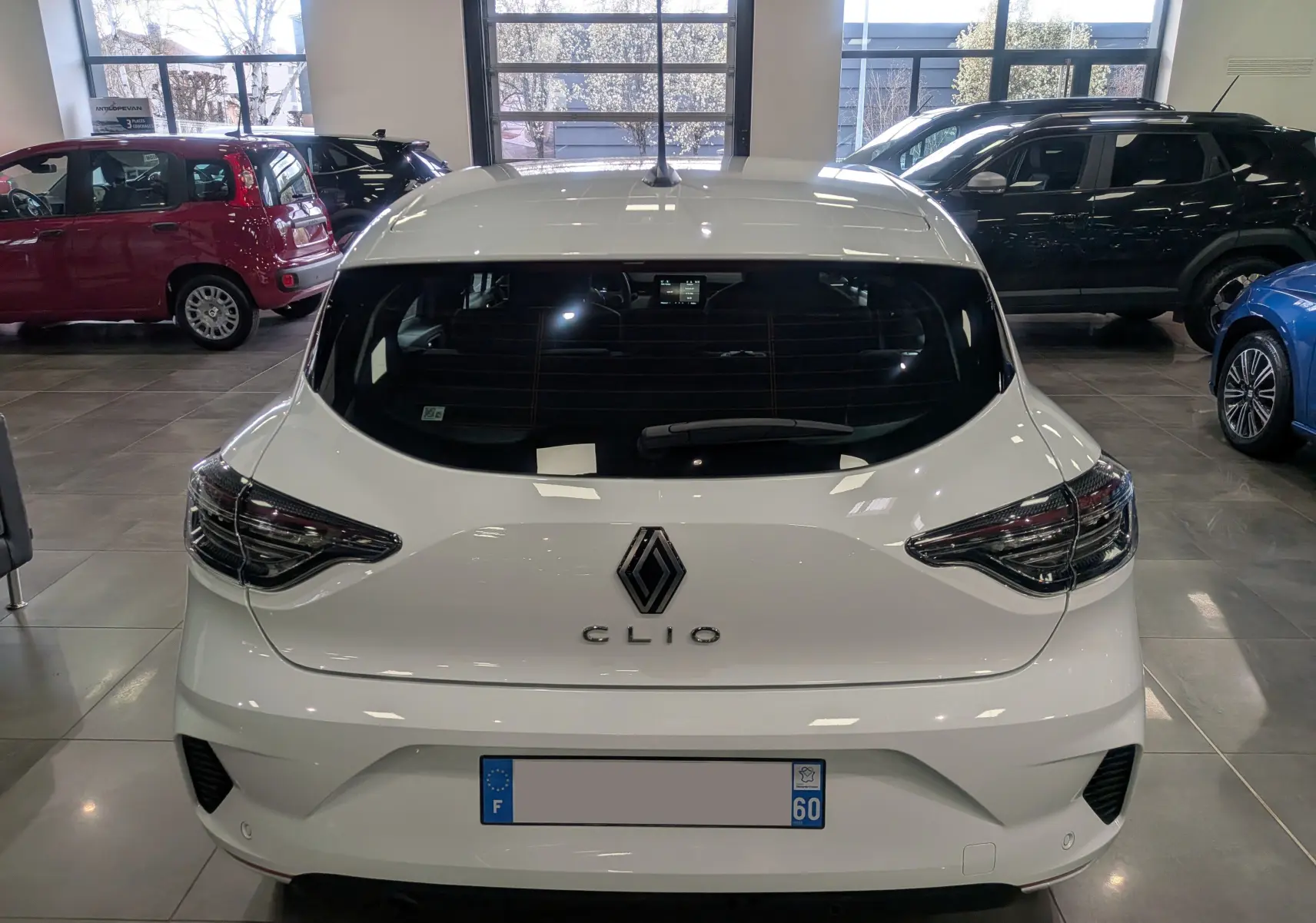 Vue arrière d'une Renault Clio V Blanc Glacier 2025 en showroom, avec feux arrière LED et logo Renault bien visibles.