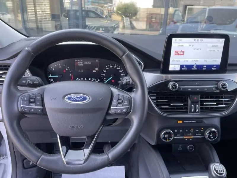 Vue intérieure du tableau de bord du Ford Kuga blanc 2020, avec volant multifonction et écran tactile central allumé.