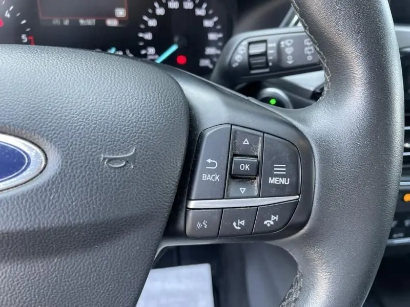 Gros plan sur les commandes du volant du Ford Kuga blanc 2020, version 2.0 EcoBlue 150 MHEV Titanium, boîte manuelle.