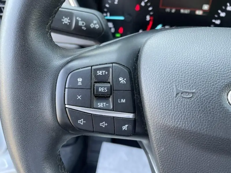 Gros plan sur les commandes au volant gauche du Ford Kuga blanc 2020, mettant en valeur les boutons de régulateur de vitesse.