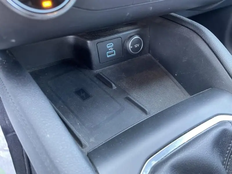 Gros plan sur la console centrale du Ford Kuga blanc 2020, montrant prise USB, port 12V et zone de recharge sans fil.
