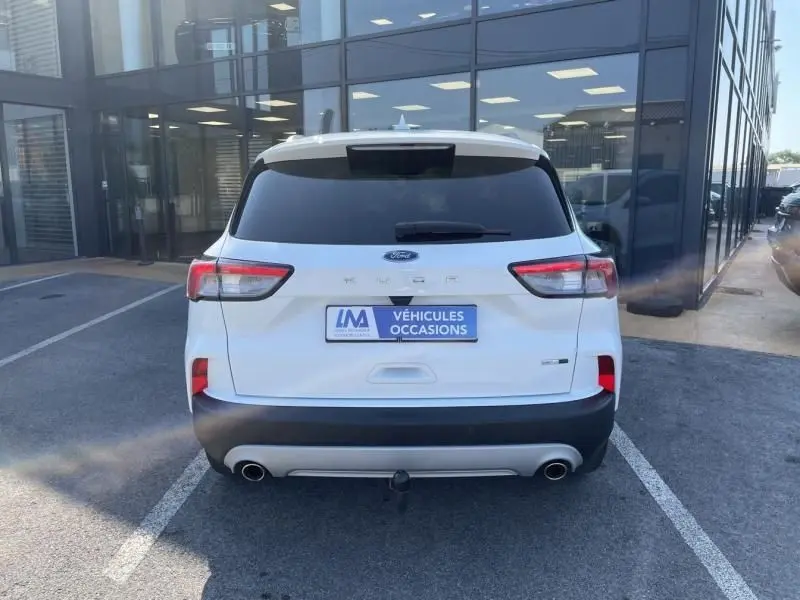Vue arrière d'un Ford Kuga blanc 2020 avec logo Ford, feux rouges et plaque d'occasion visible sur parking.