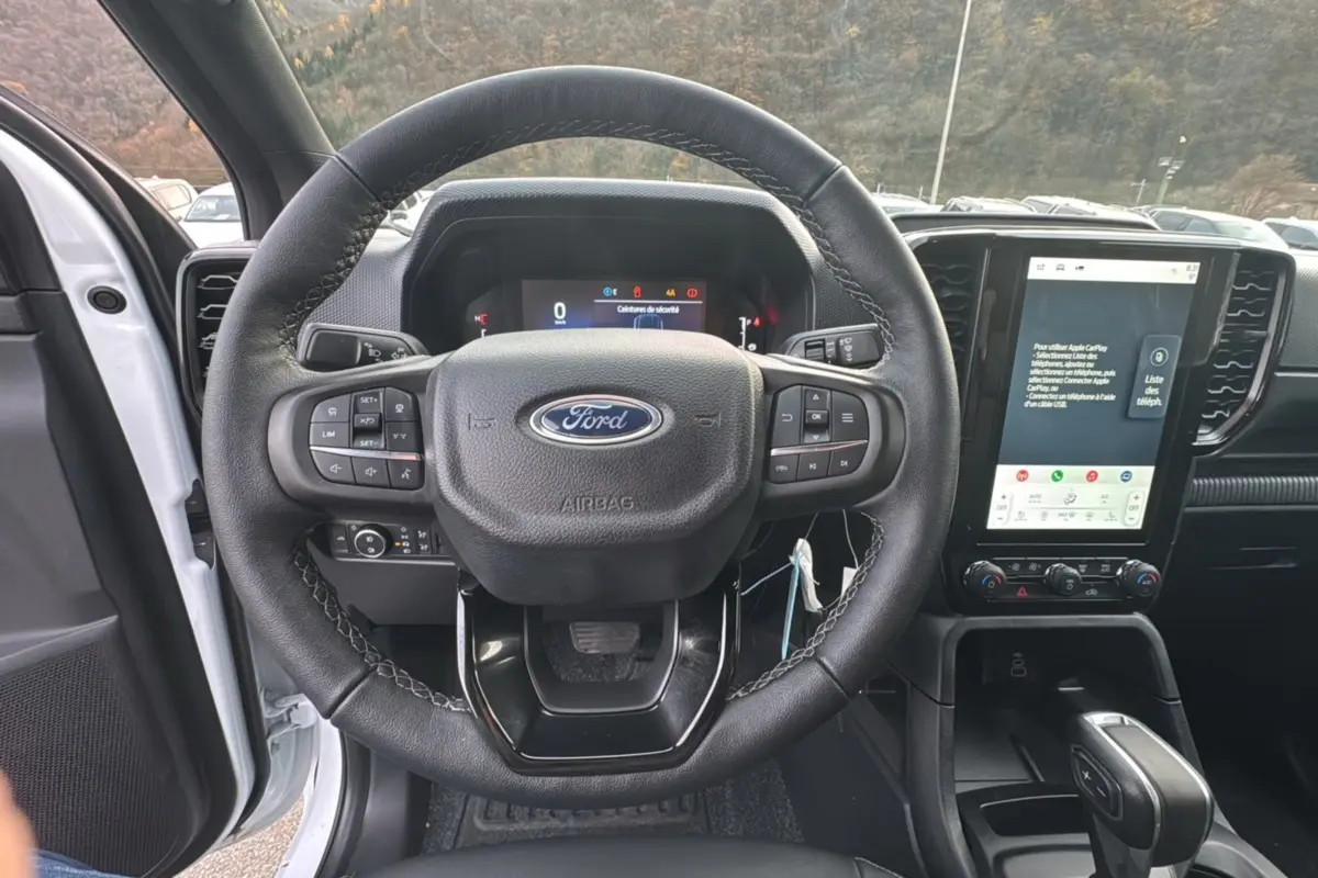 Vue intérieure centrée sur le volant cuir multifonctions d'un Ford Ranger blanc glacier avec écran tactile vertical.