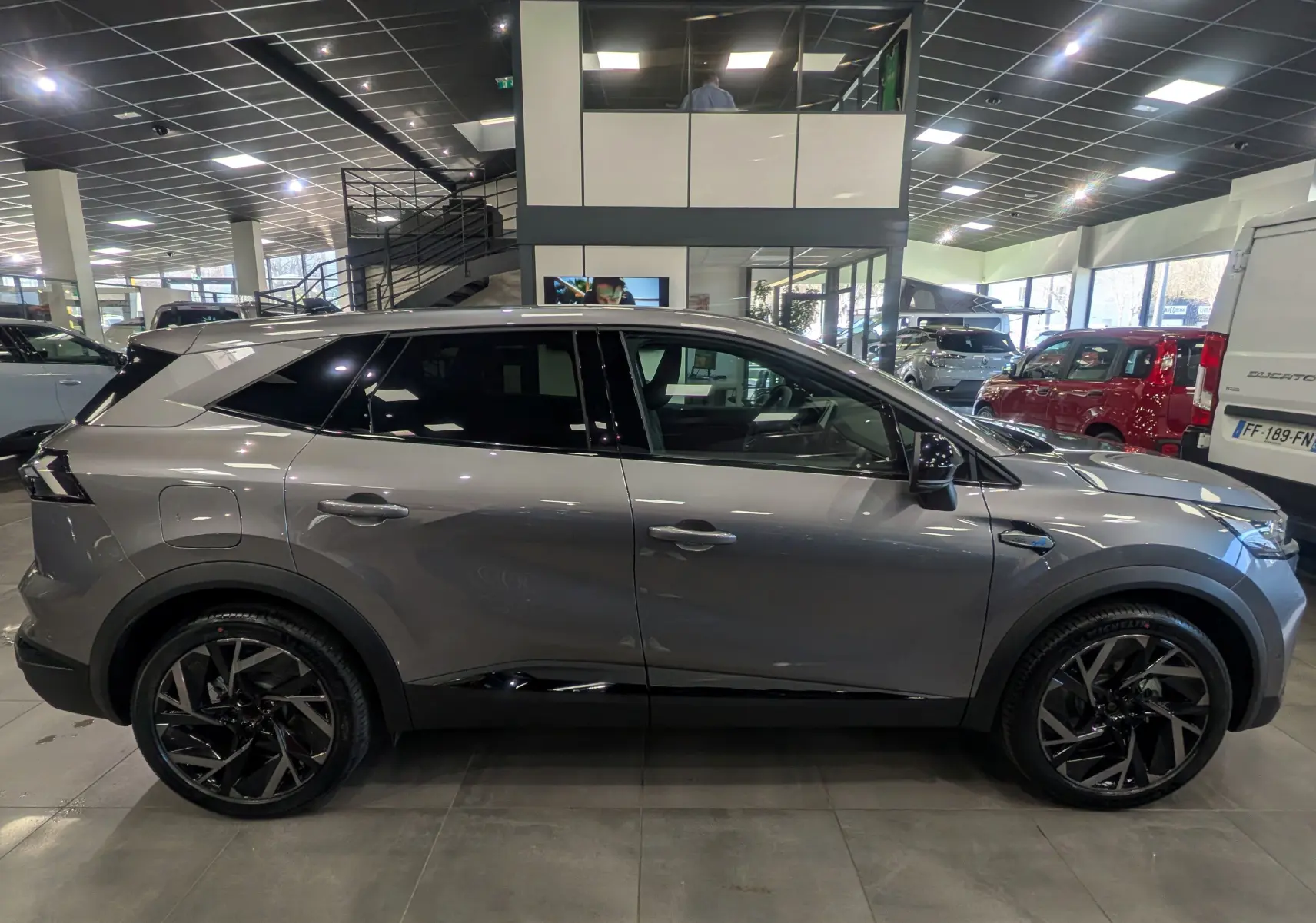 Profil droit du Renault SYMBIOZ E-TECH Full Hybrid gris Cassiopé, avec jantes noires et toit noir en showroom.