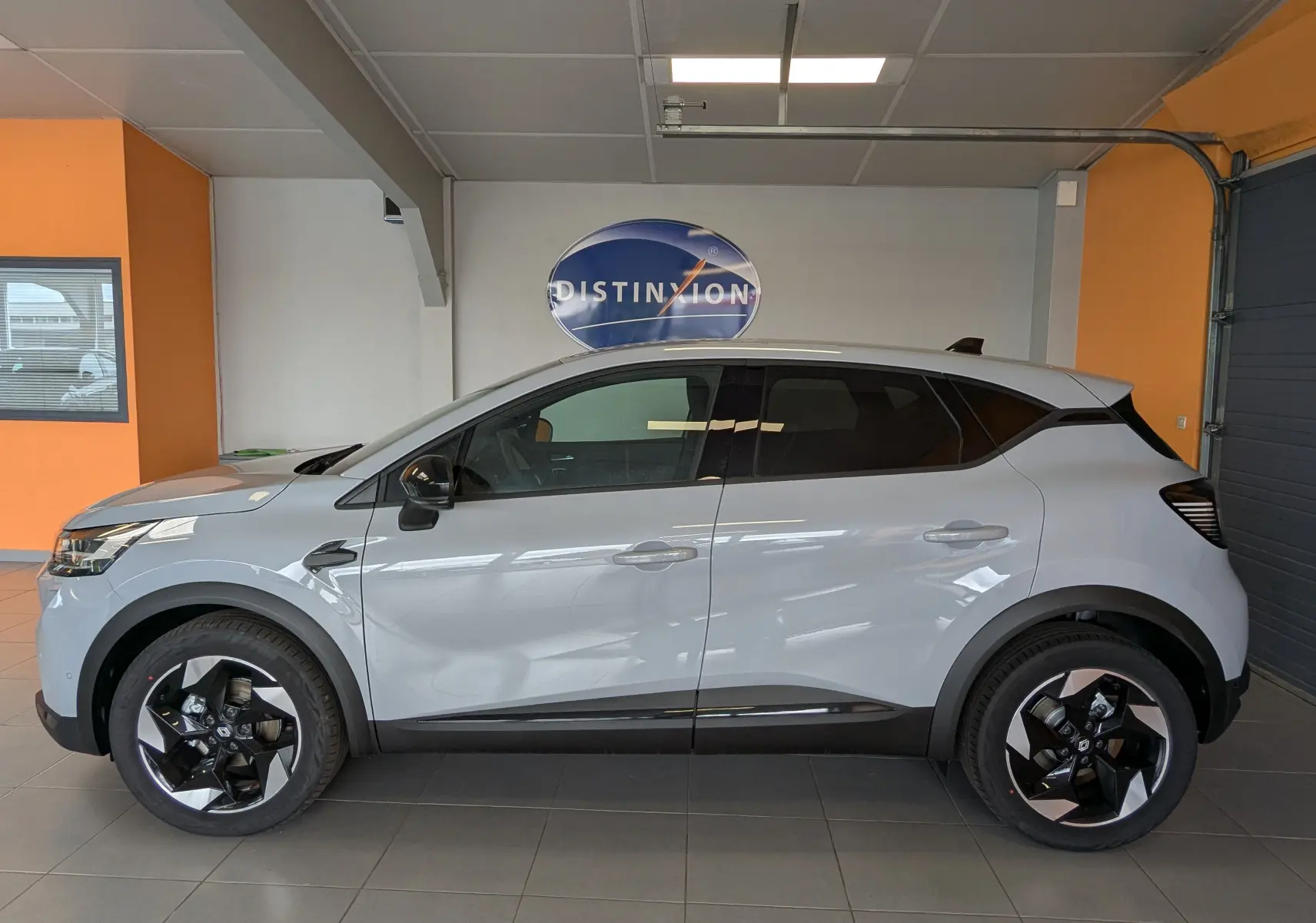 Profil côté gauche d'un Renault Captur gris zinc 2025 avec jantes alliage 18'' bicolores en intérieur showroom.