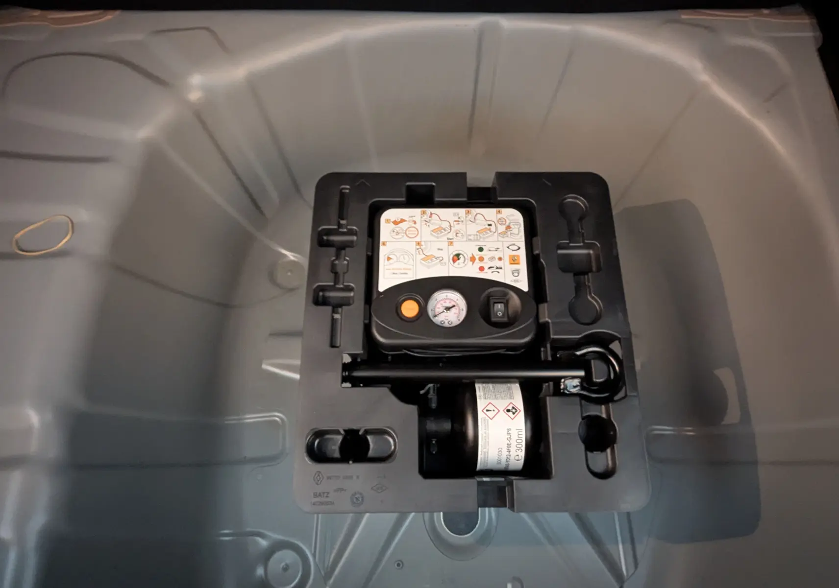 Gros plan sur le kit de gonflage et de réparation des pneumatiques dans le coffre du Renault Captur gris zinc 2025.
