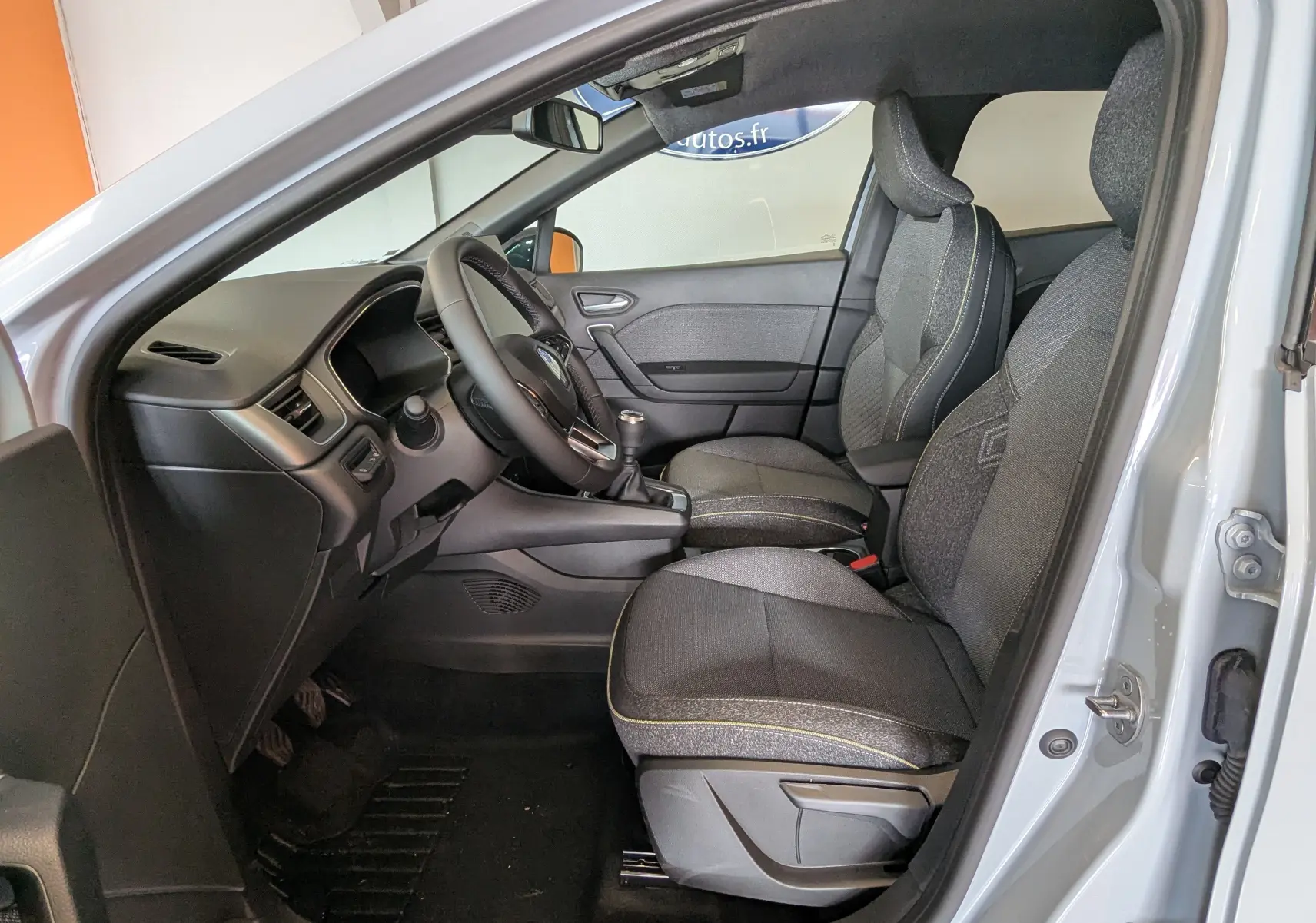 Intérieur côté conducteur du Renault Captur 2025, sièges tissu gris avec surpiqûres jaunes et volant tissu.