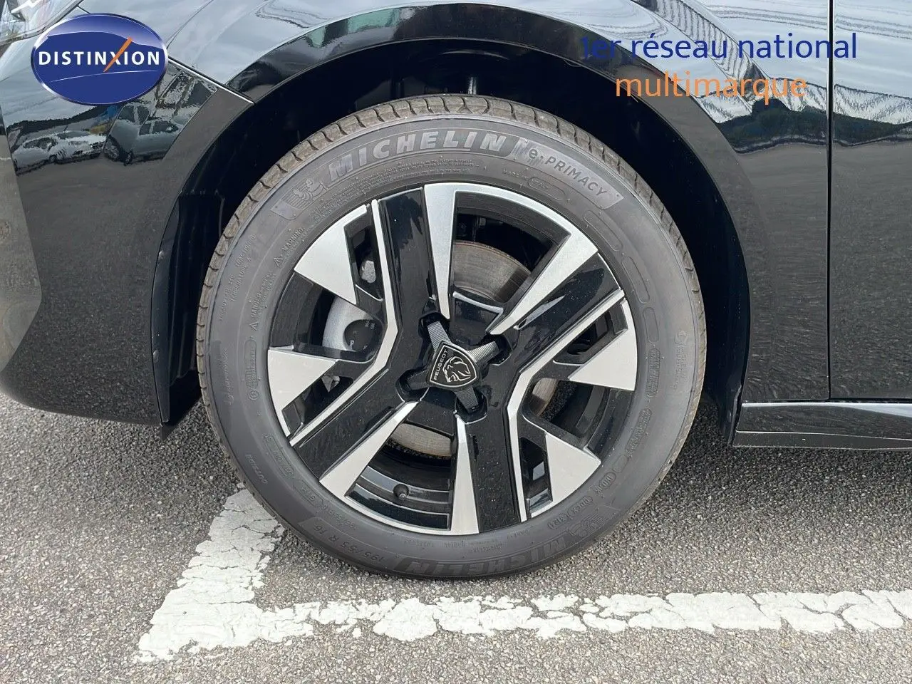 Gros plan sur la roue avant gauche d'une Peugeot 208 noire Perla Metal avec jante alliage bicolore moderne.