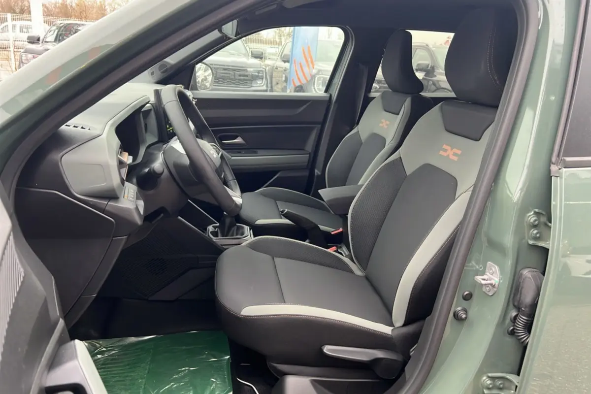 Intérieur côté conducteur du Dacia Duster 2025 kaki lichen, montrant les sièges sport avec logo orange et tableau de bord moderne.