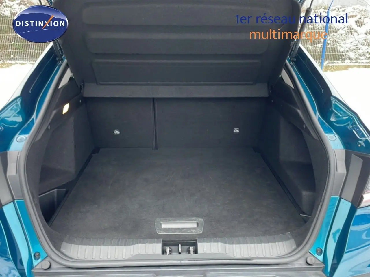 Coffre ouvert vu de l'arrière d'un Renault Arkana bleu Zanzibar métal, montrant l'espace de chargement vide.