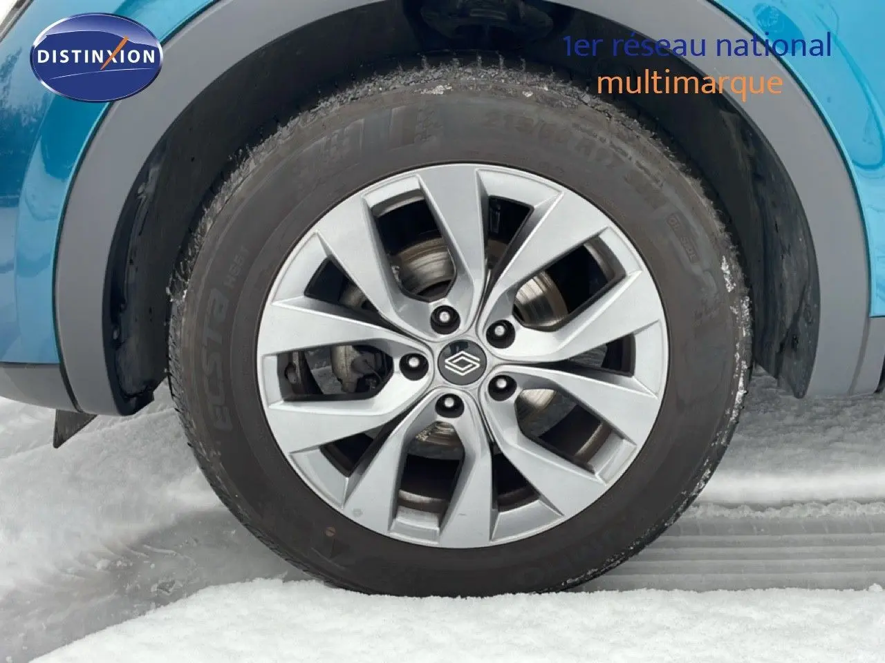 Gros plan sur la roue avant gauche avec jante argentée du Renault Arkana bleu Zanzibar métal sur neige.