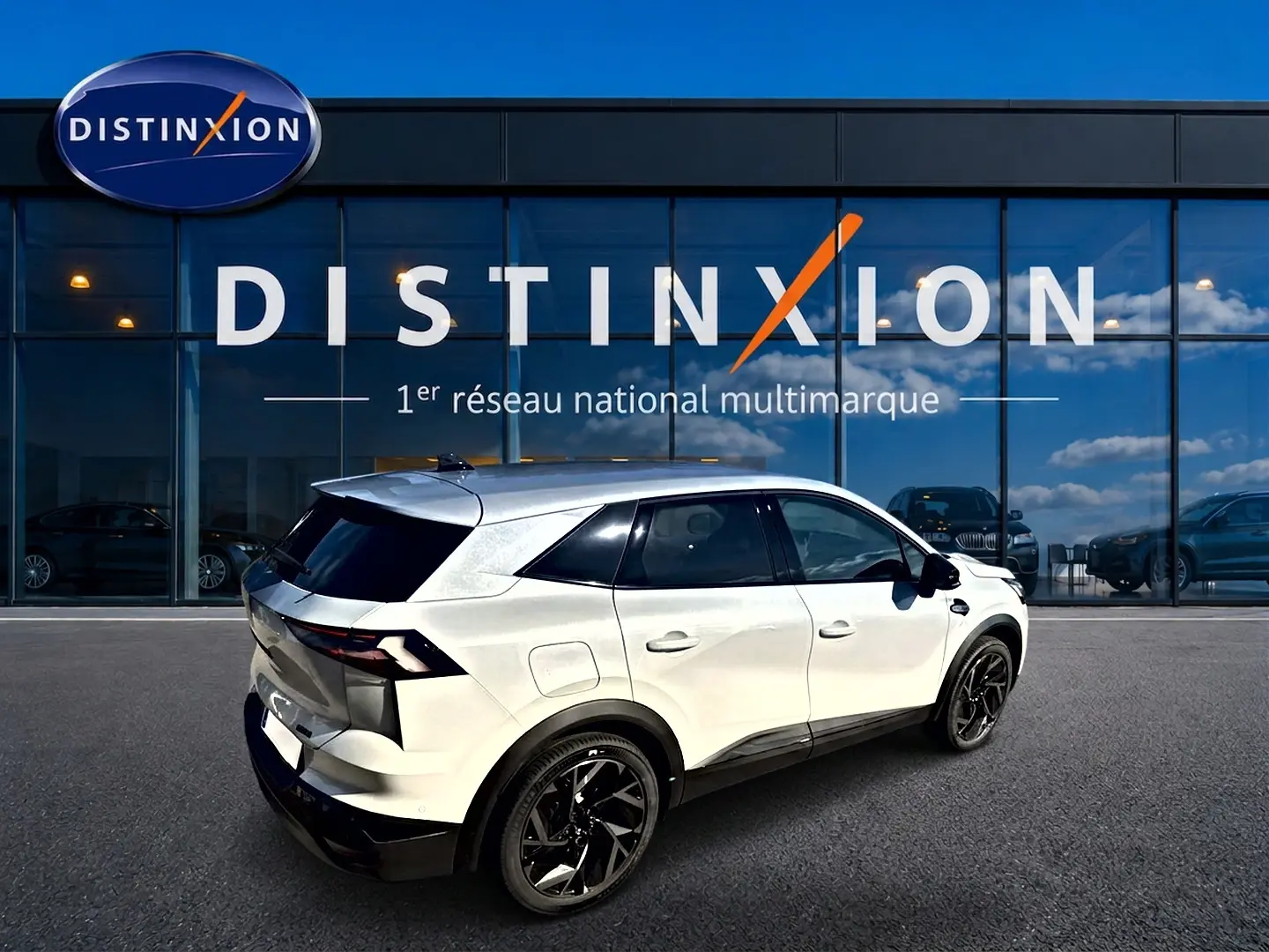 Vue 3/4 arrière droite du Renault Symbioz blanc nacré avec jantes noires et toit noir devant un bâtiment vitré Distinxion.