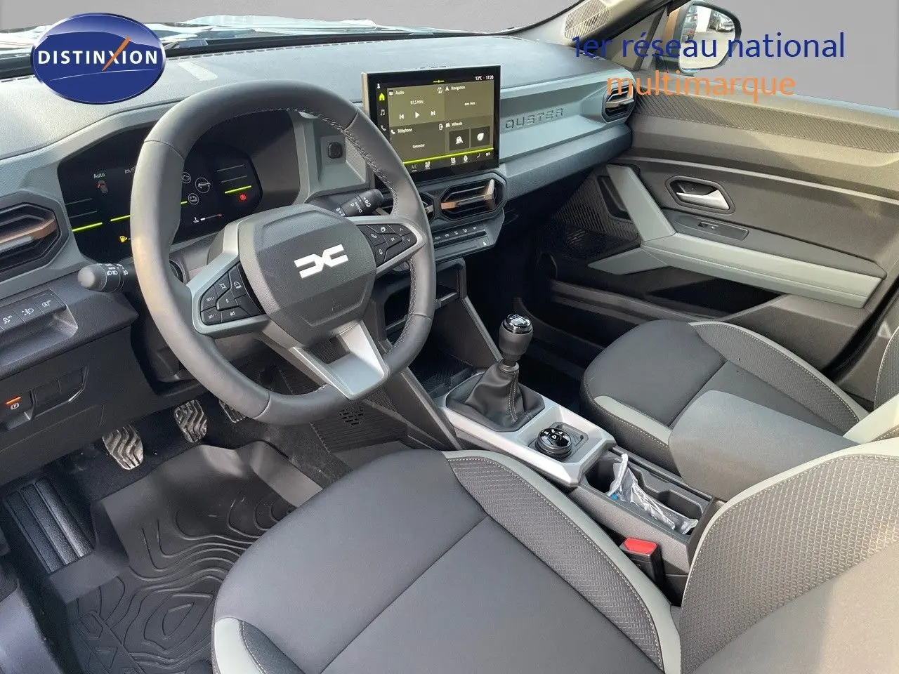 Intérieur du Dacia Duster 2024 noir métal, vue côté conducteur montrant volant, tableau de bord digital et levier de vitesse manuel.