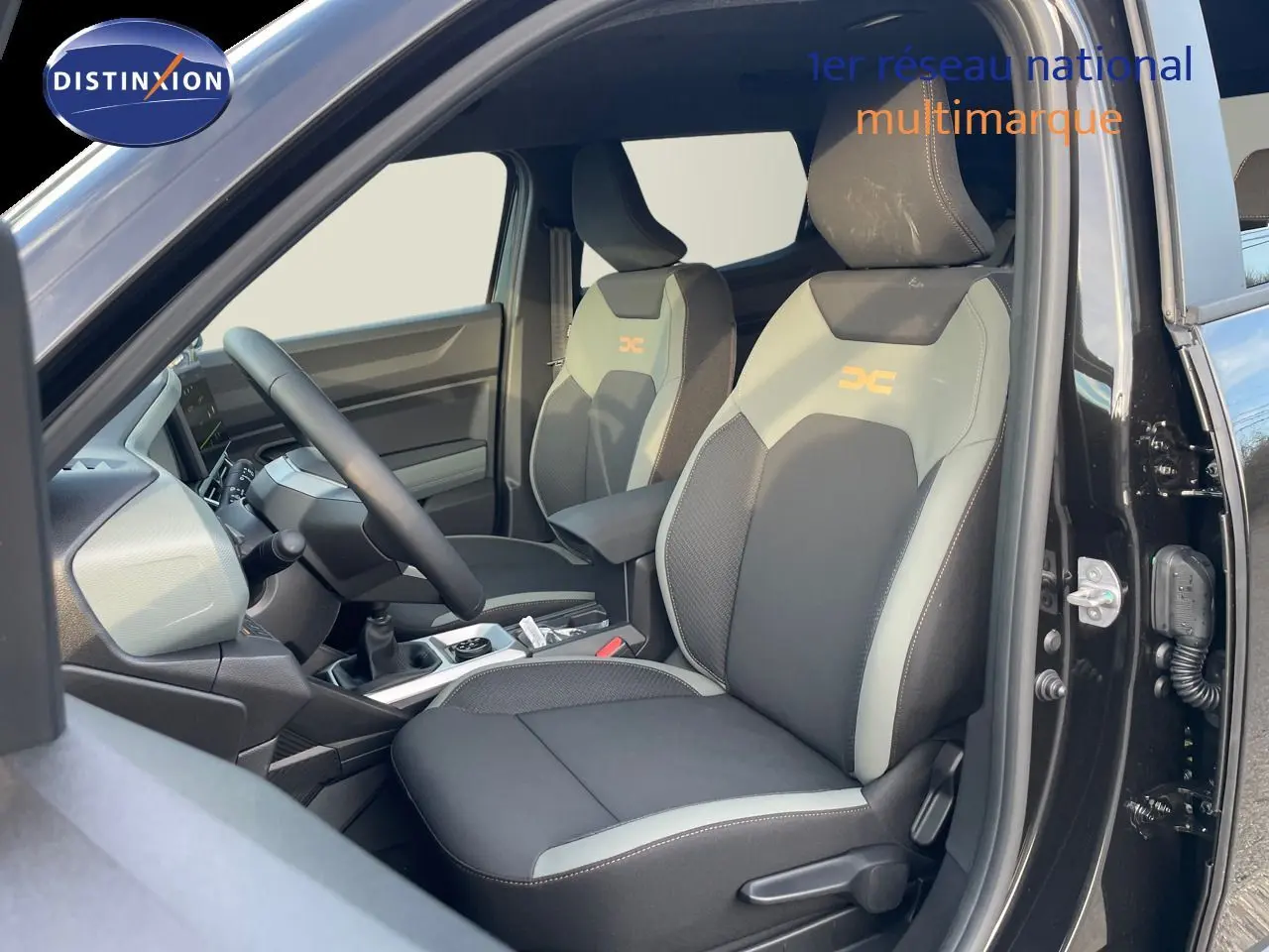 Vue intérieure côté conducteur du Dacia Duster 2024 noir métal, sièges bi-ton gris et noir avec logo orange DC.
