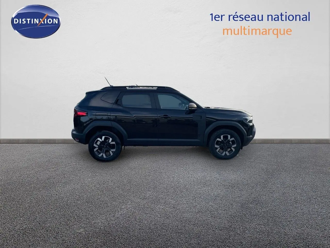 Profil droit d'un Dacia Duster 2024 noir métal avec jantes bi-ton et barres de toit visibles sur fond neutre.