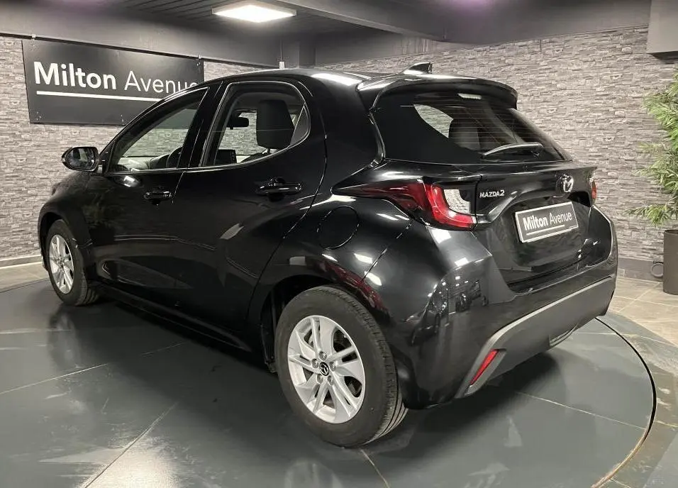 Vue 3/4 arrière droite d'une Mazda2 noire 2023 avec becquet de toit et jantes alliage argentées dans un showroom.