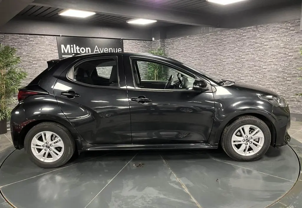 Profil droit de la Mazda2 noire 2023 en hybride essence, avec jantes alliage et becquet de toit visible.