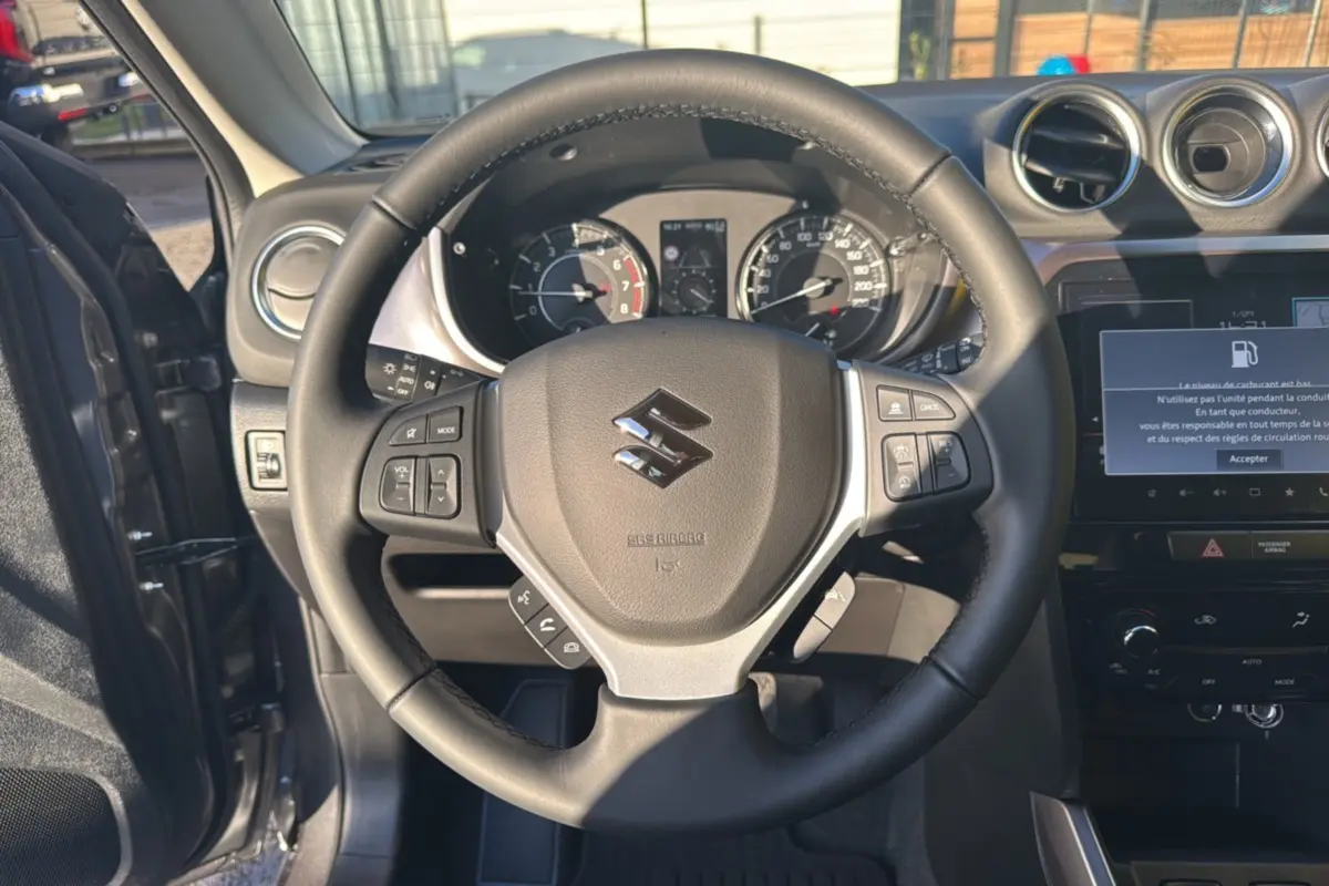 Vue intérieure centrée sur le volant cuir multifonctions du Suzuki Vitara Hybrid 110 Privilege AllGrip gris Titan.