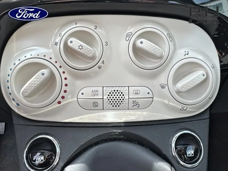 Panneau de commandes de climatisation beige dans une Fiat 500 Lounge noire, vue frontale rapprochée.