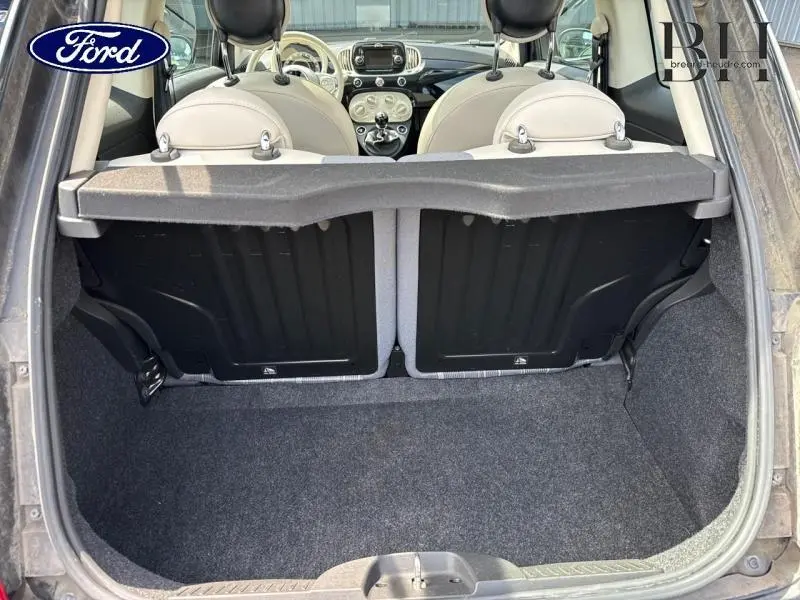 Coffre ouvert d'une FIAT 500 Lounge noire, vue arrière montrant l'intérieur clair et la banquette rabattue partiellement.
