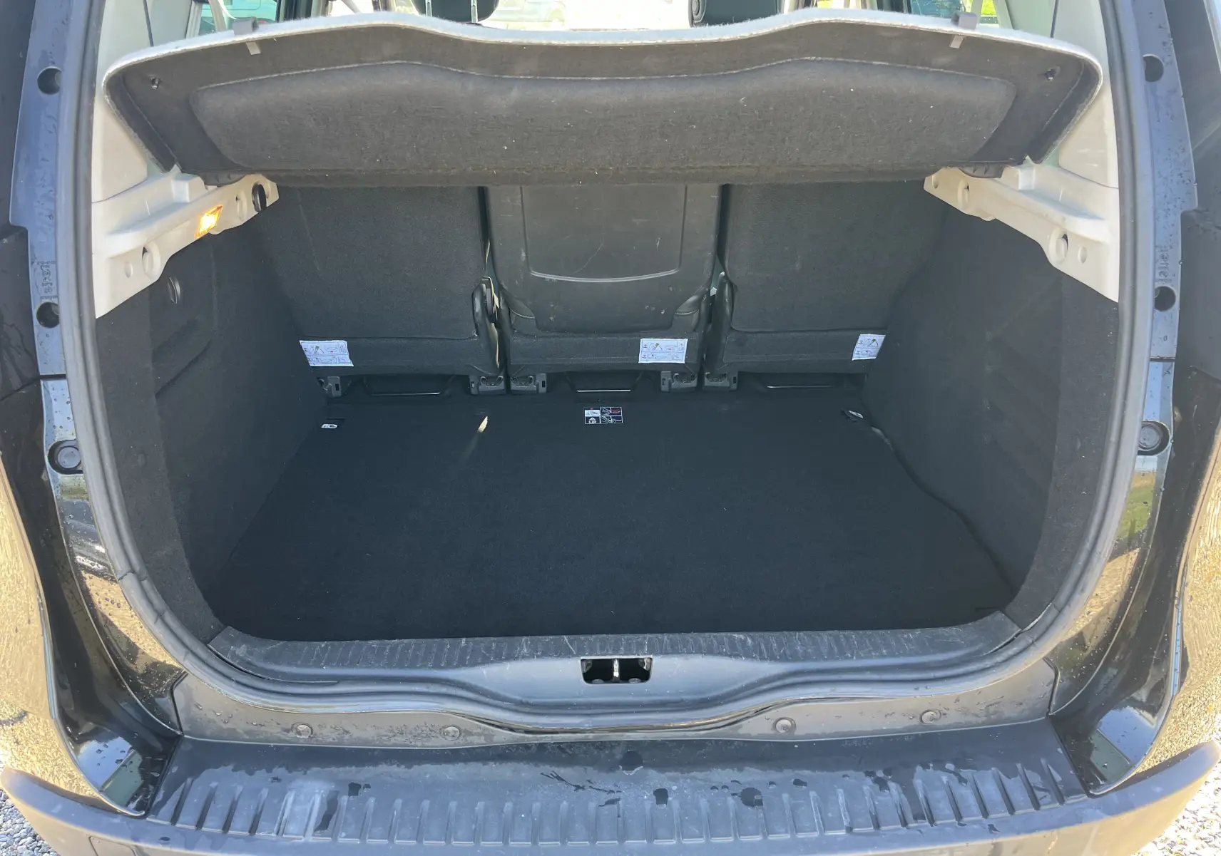 Coffre ouvert vu de l'arrière d'un Renault Scénic III noir, montrant l'espace de chargement et les dossiers des sièges arrière.