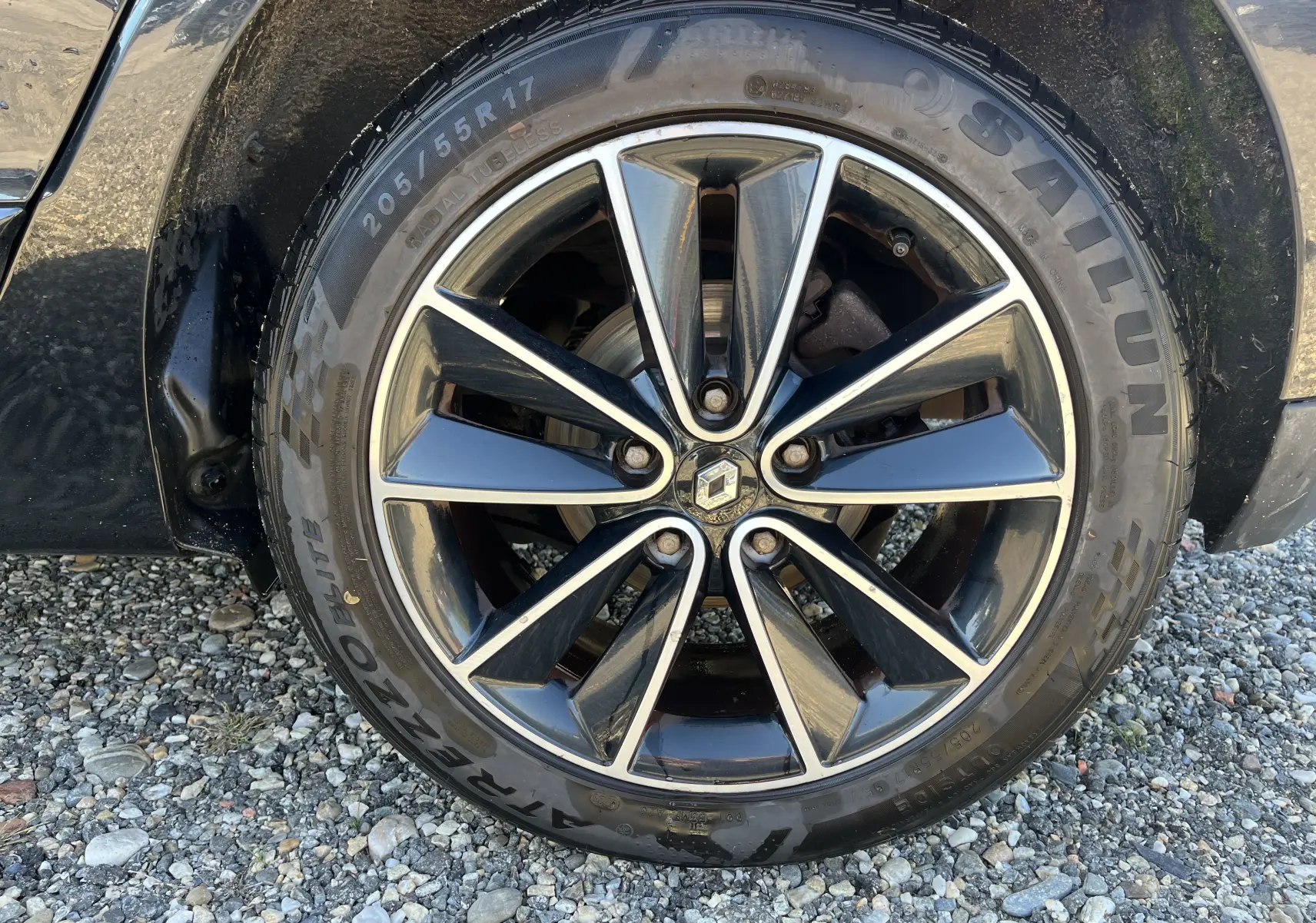 Gros plan sur la roue avant gauche noire du Renault Scenic III 1.5 DCI 110 CH avec jante alliage bicolore et logo Renault central.