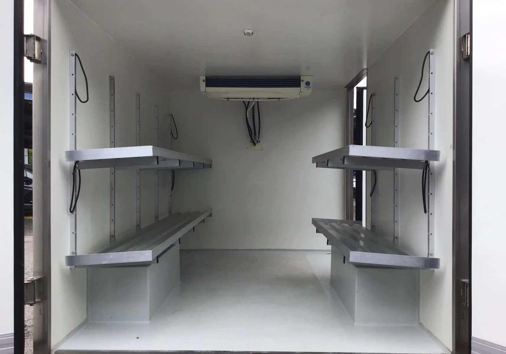 Intérieur de la caisse frigorifique blanche du Renault Trafic Planche cabine, vue arrière avec étagères métalliques et groupe froid au plafond.