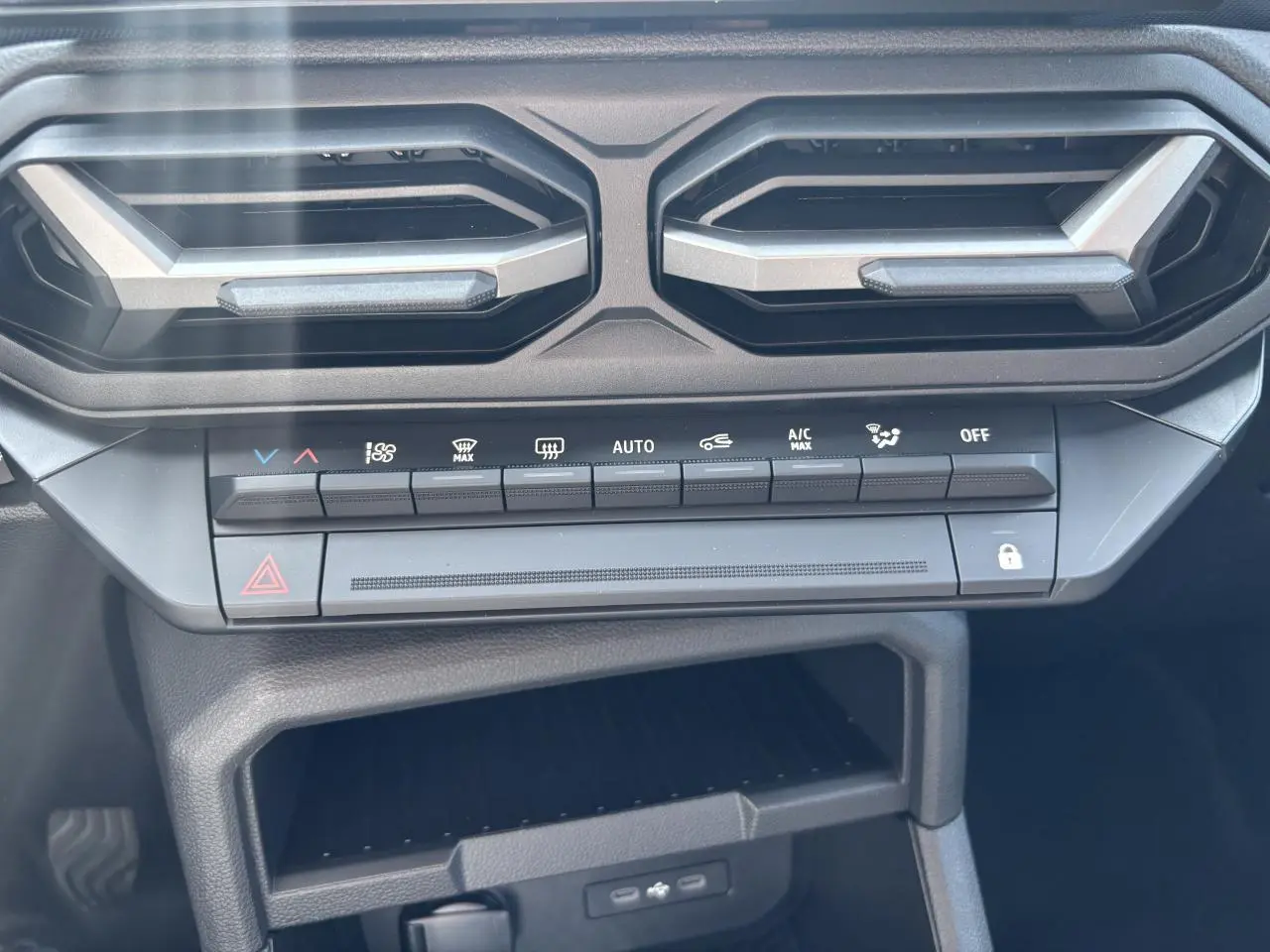 Gros plan sur la console centrale du Dacia Duster 2025, avec commandes climatisation et aérateurs hexagonaux noirs.