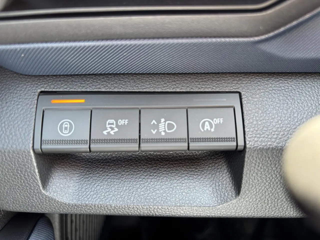 Gros plan sur les boutons de commande noirs du tableau de bord du Dacia Duster 2025, finition Journey, avec témoin orange allumé.