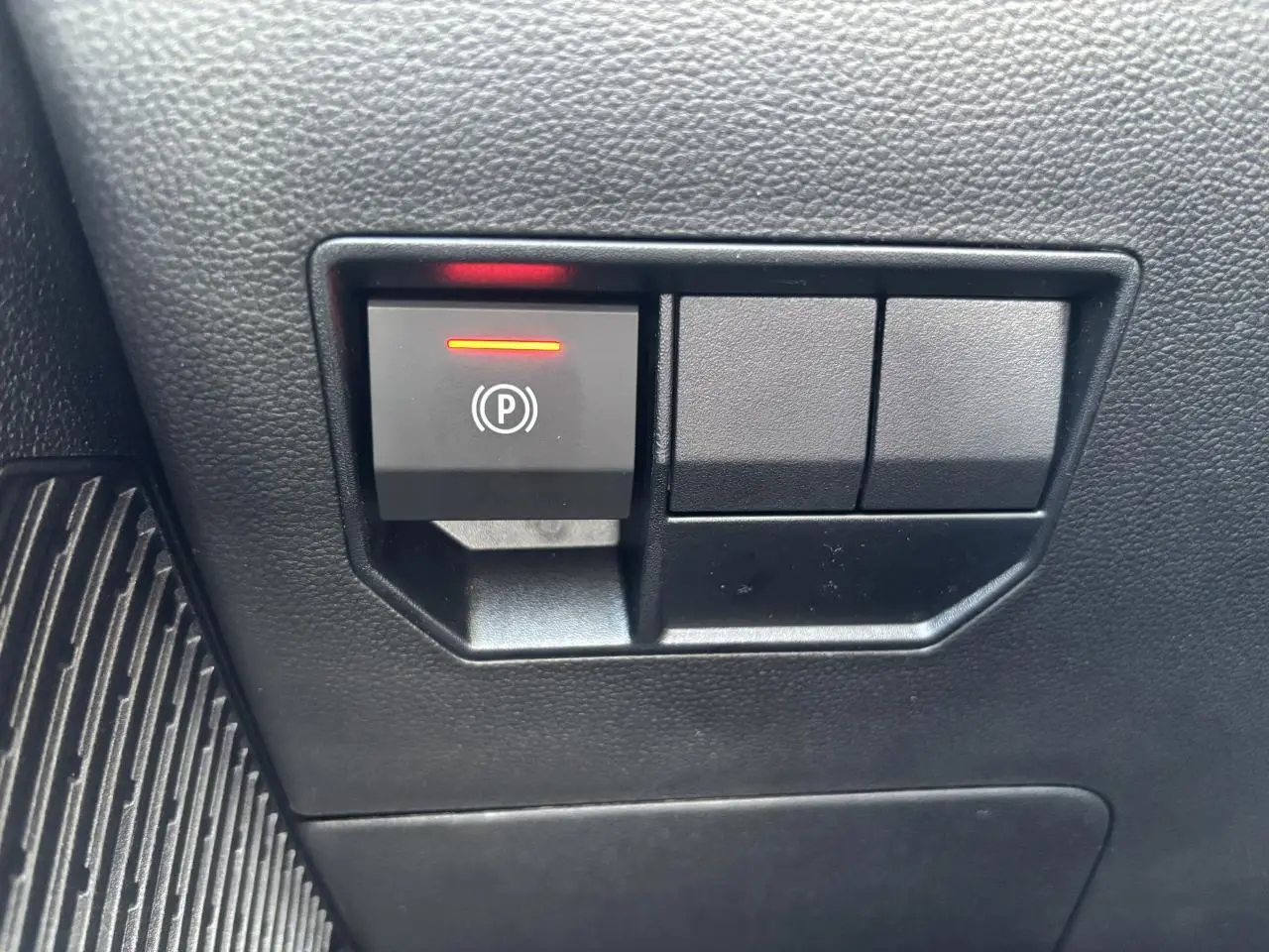 Gros plan sur le bouton de frein de stationnement électrique avec témoin rouge dans l'habitacle du Dacia Duster 2025.